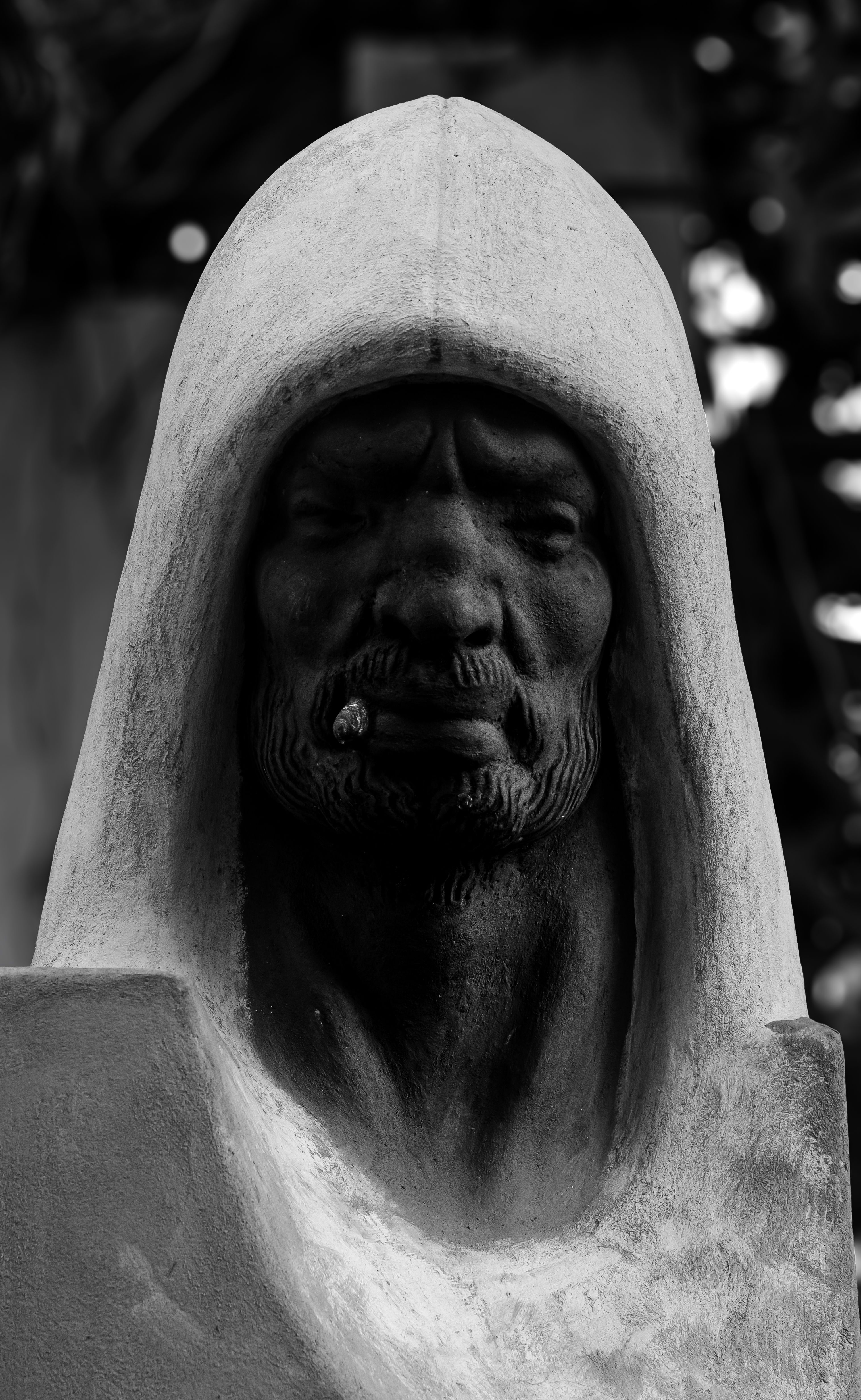 Monochrome close-up of a hooded statue in artistic shadows.