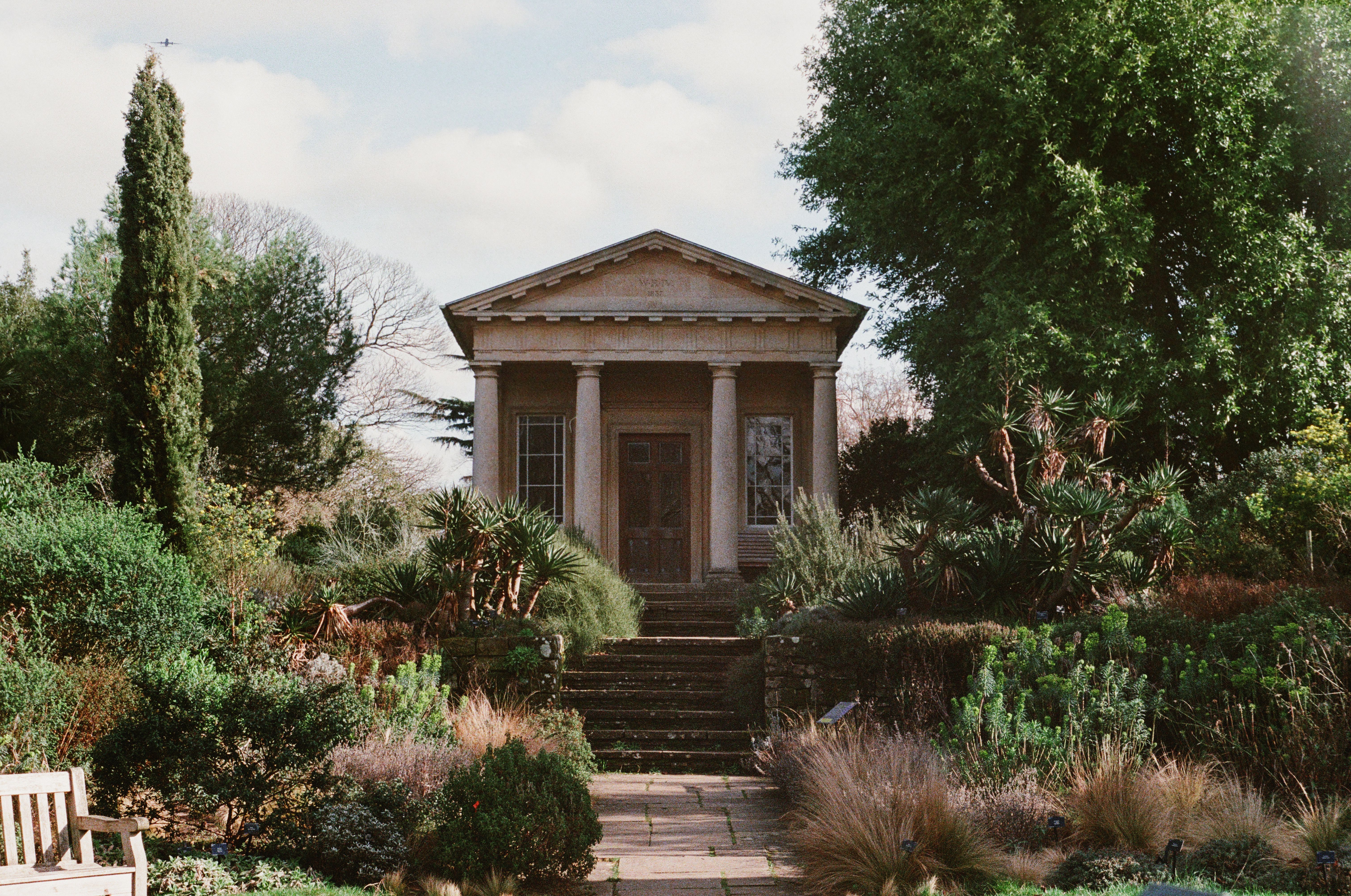An elegant garden pavilion amidst lush greenery under a bright sky, exuding tranquility.