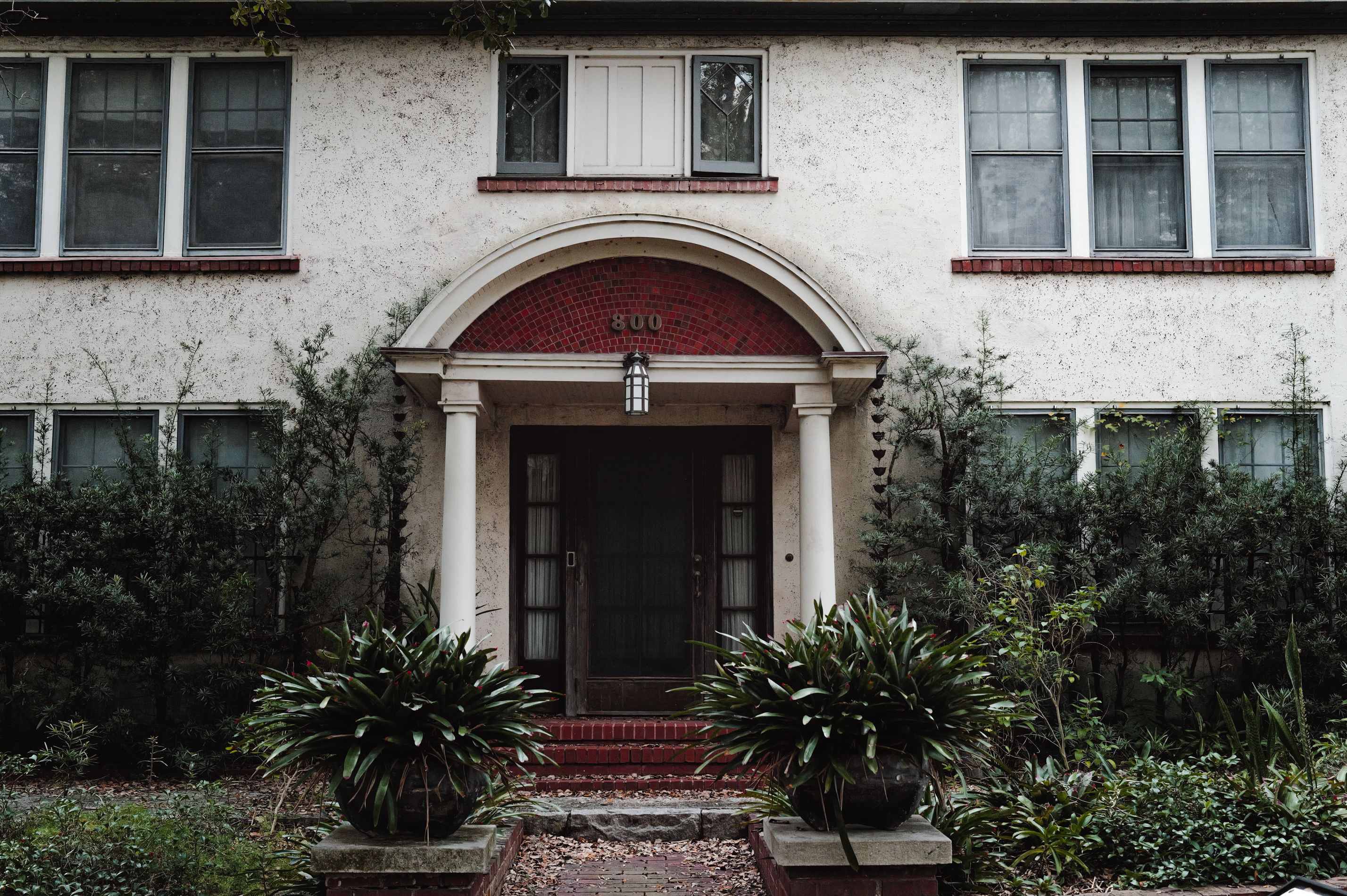 Elegant entrance of a vintage residential building framed by greenery and archway.