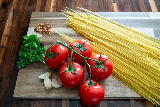 A vibrant still life of fresh tomatoes, parsley, garlic, and spaghetti on a wooden surface.