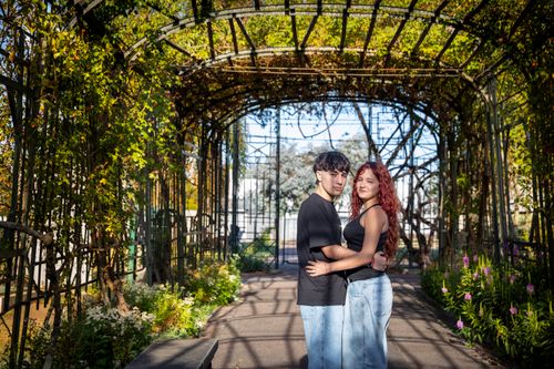 Free A couple sharing an embrace under a sunlit garden archway with vibrant greenery. Stock Photo