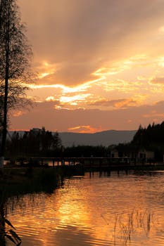 Peaceful sunset scene over a calm lake with reflections and silhouetted trees.