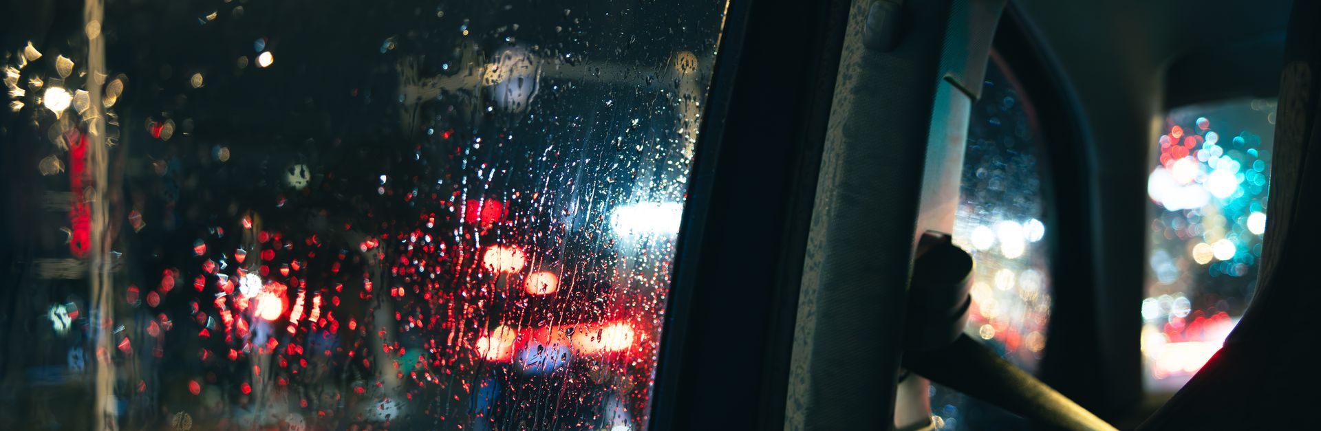 Rainy city lights seen through a wet car window, capturing urban nightlife ambiance.