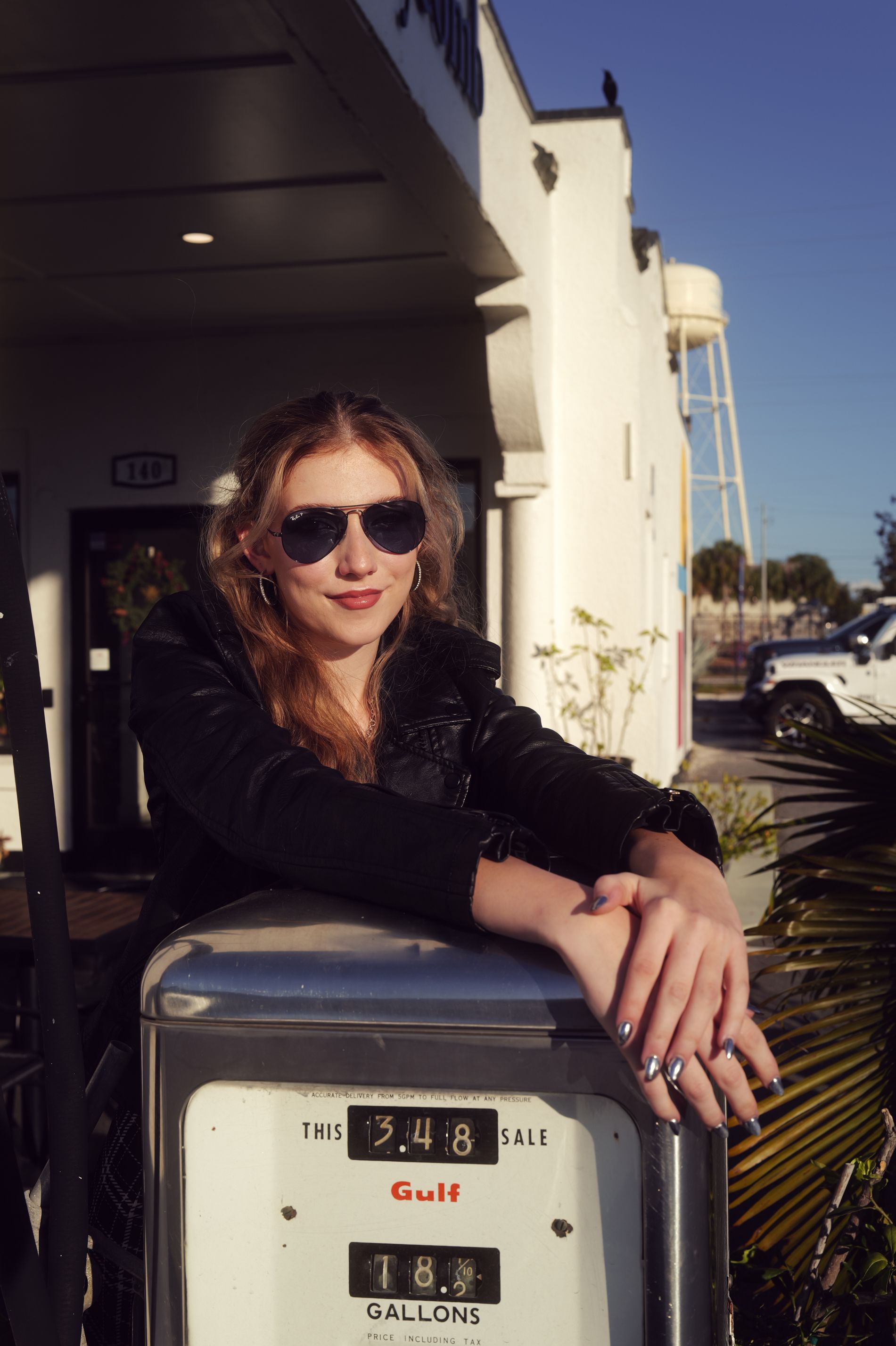 A stylish woman in sunglasses leans on a vintage gas pump at a retro-themed station - historic gas stations