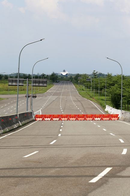 Photo by Jeffry Surianto Empty highway blocked by orange barricades with distant building under blue sky.