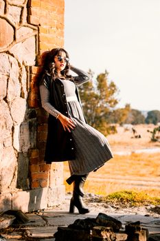 Trendy woman leans against a rustic stone and brick wall on a sunny day outdoors.