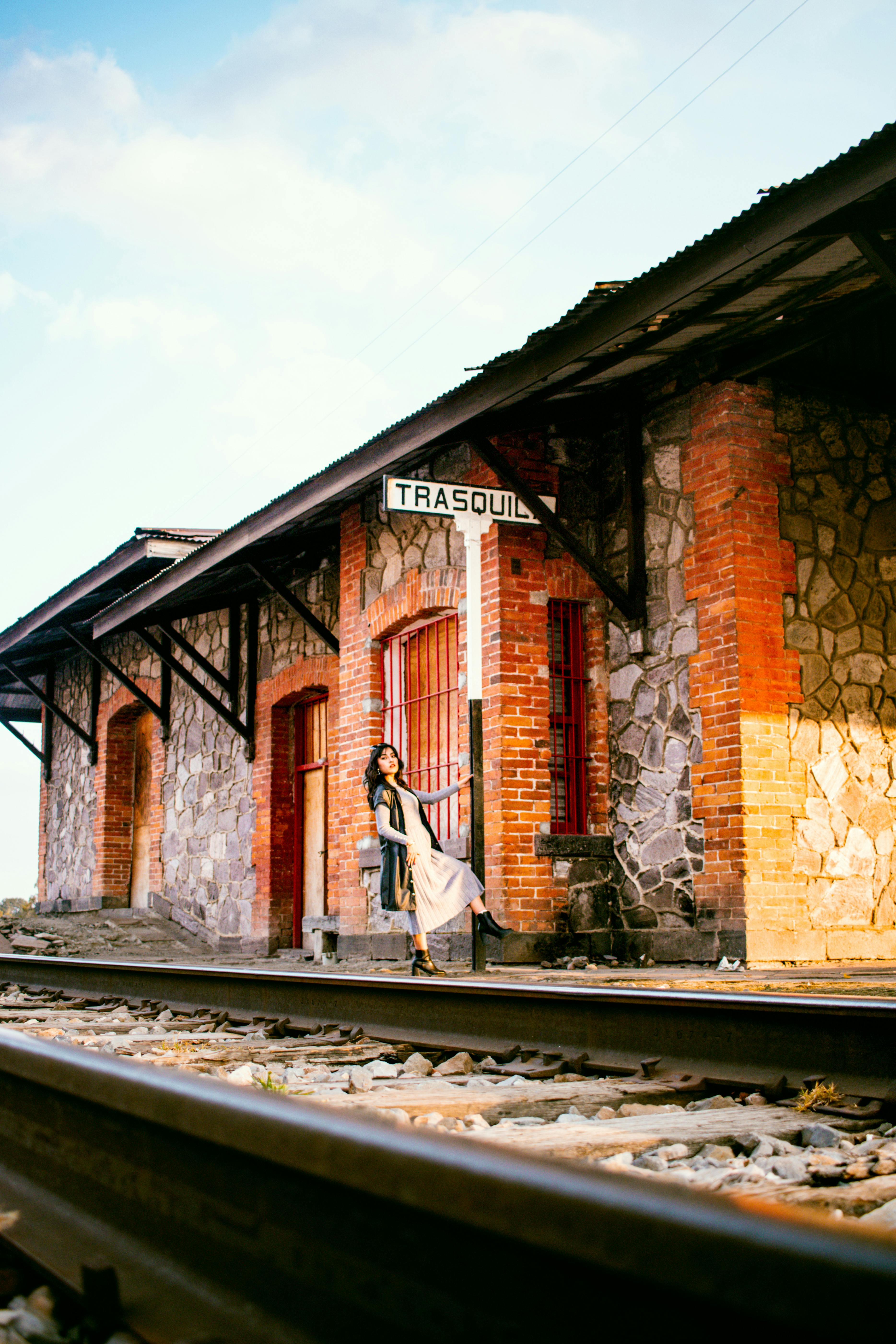 бесплатная Женщина в платье танцует на железнодорожных путях рядом с простой каменной железнодорожной станцией. Стоковое фото