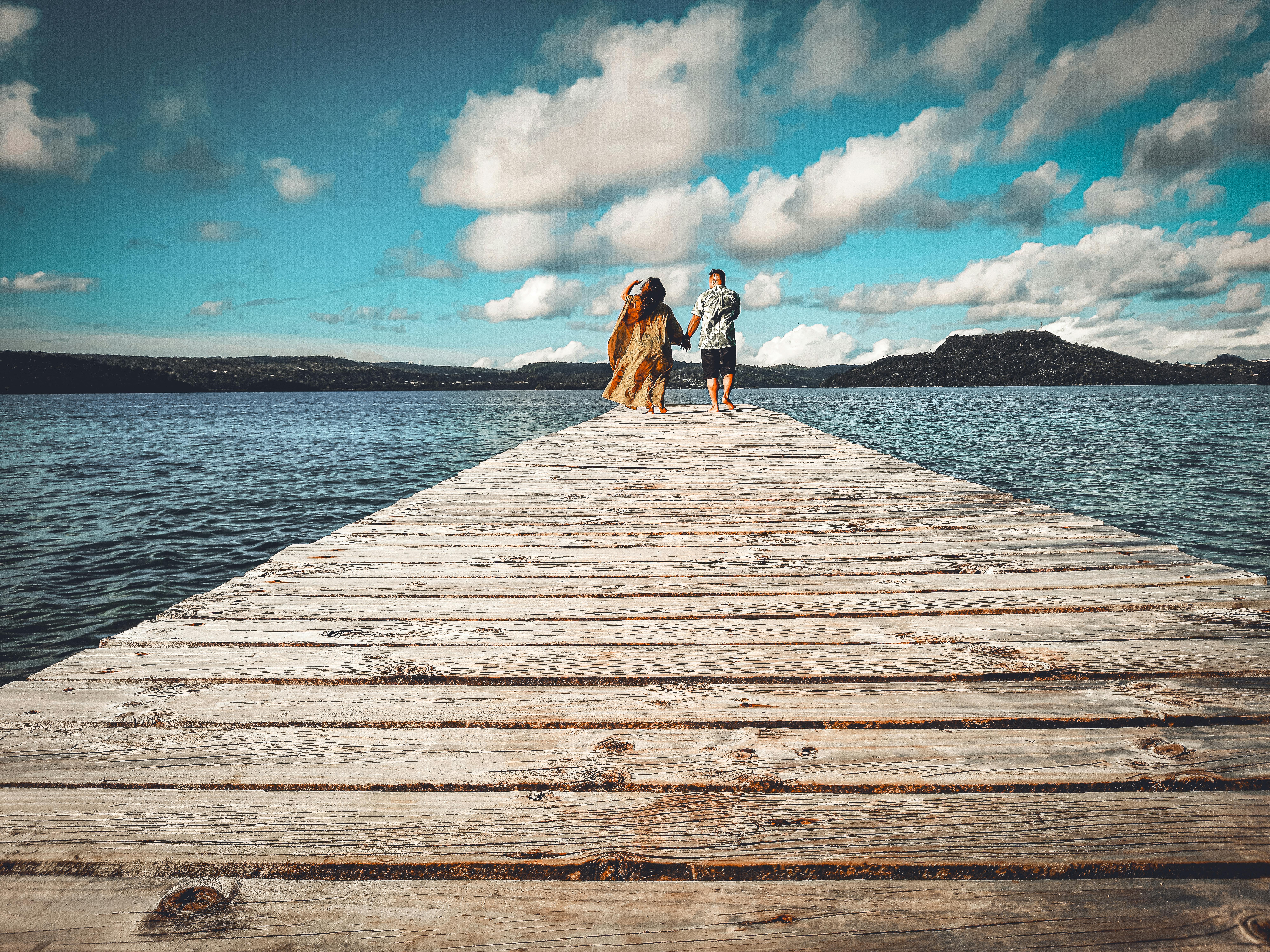 無料 穏やかな水と美しい景色を見渡せる木製の桟橋で夏の散歩を楽しむカップル。 写真素材