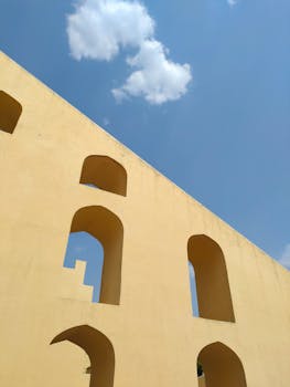 Yellow architectural structure with arches under blue sky and clouds.