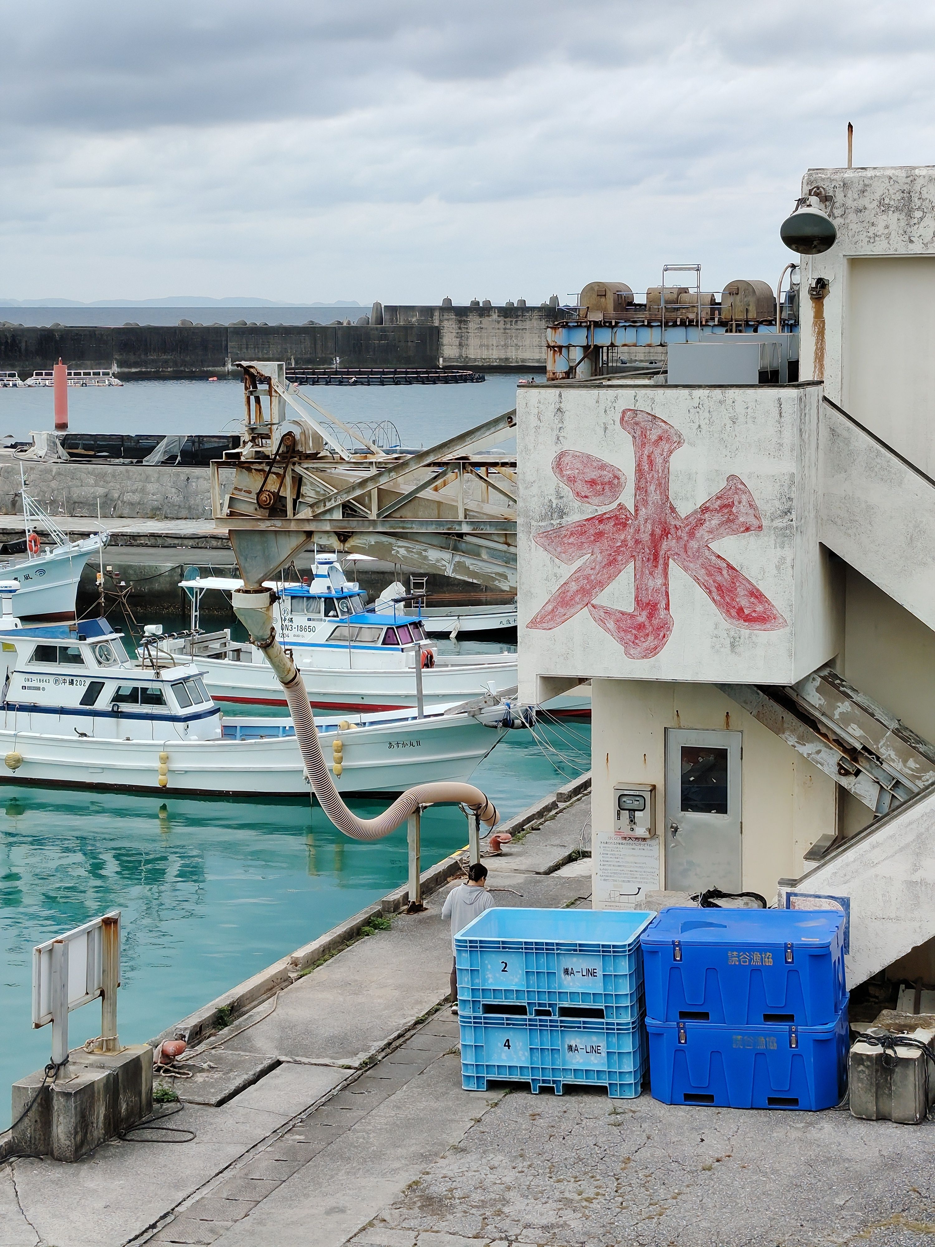 A serene fishing port with docked boats and a storage warehouse featuring vibrant signage.