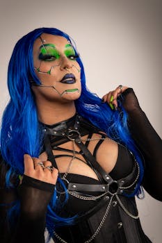 A stylish cyberpunk woman with blue hair and artistic green makeup posing confidently.