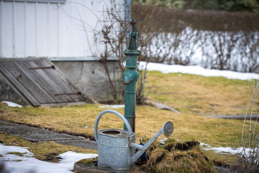 Rustic garden scene with a vintage water pump and watering can during winter in Jönköping, Sweden.
