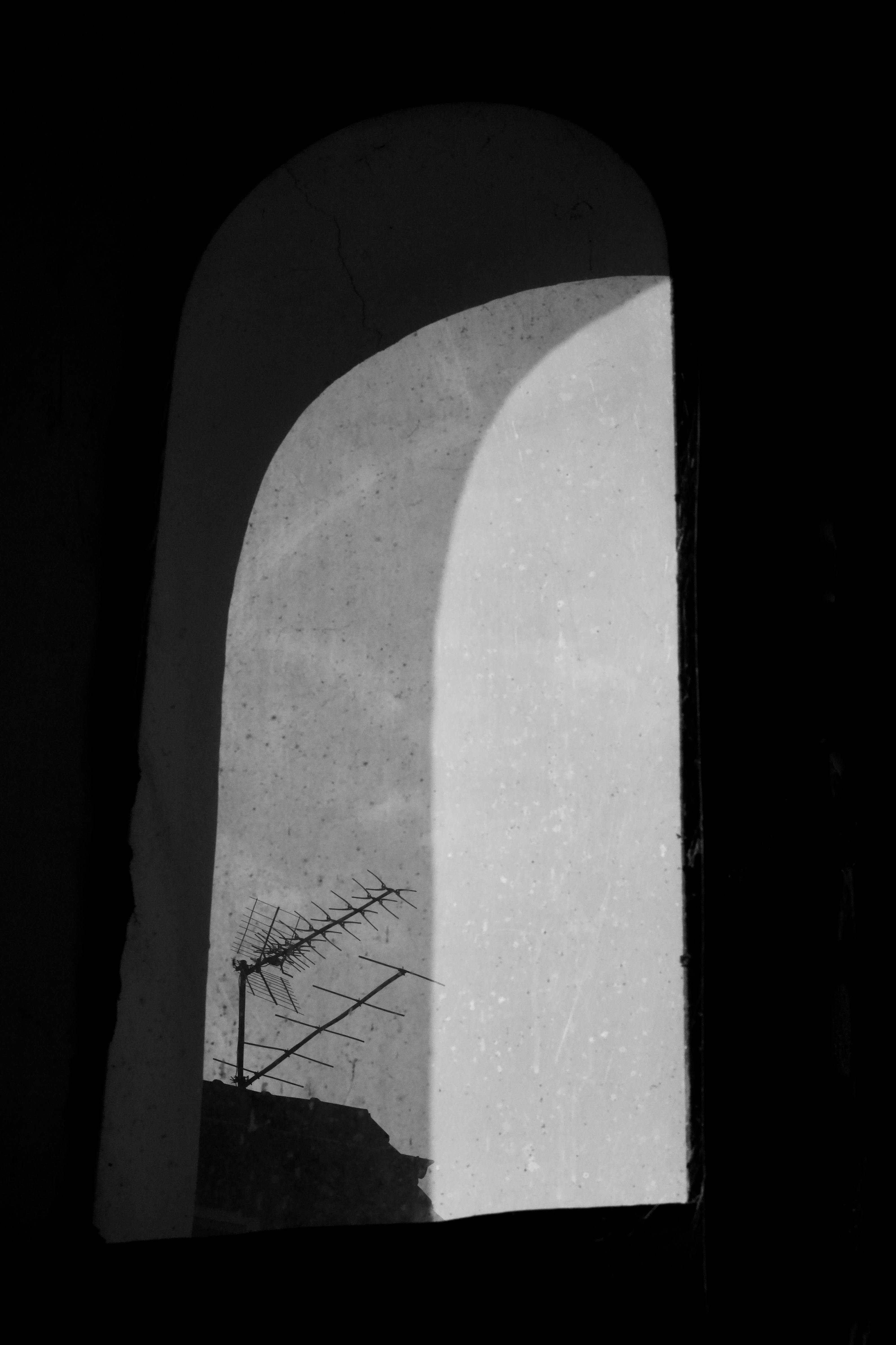 gratis Artistieke zwart-witfoto van een raam met uitzicht op een antenne, waarop dramatische schaduwen te zien zijn. Stockfoto