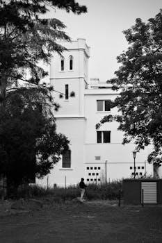 Monochrome image of a historical tower with surrounding trees and a walking figure, evoking a classic feel.