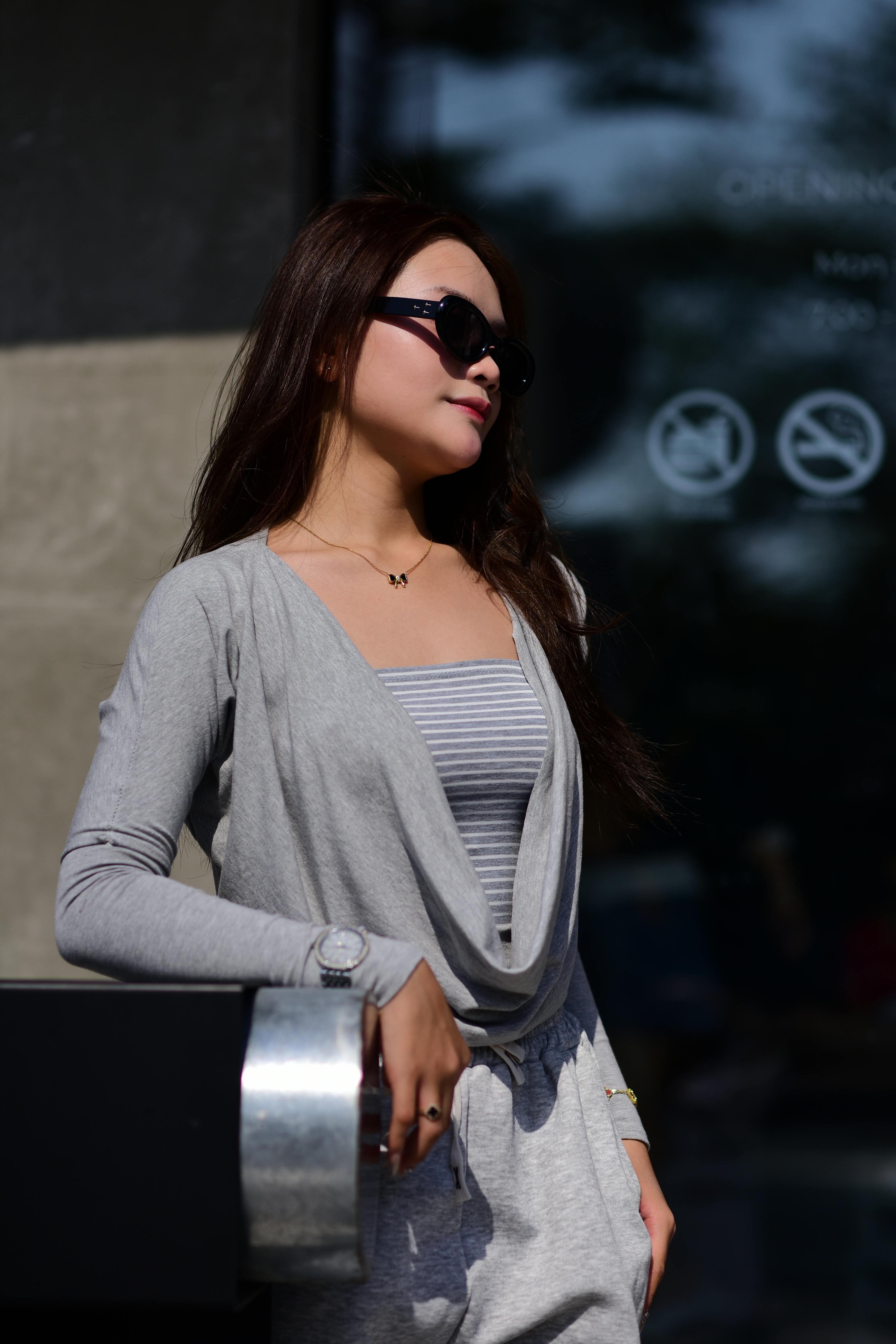 Free Fashionable woman in sunglasses poses confidently outdoors, showcasing casual chic style in urban environment. Stock Photo