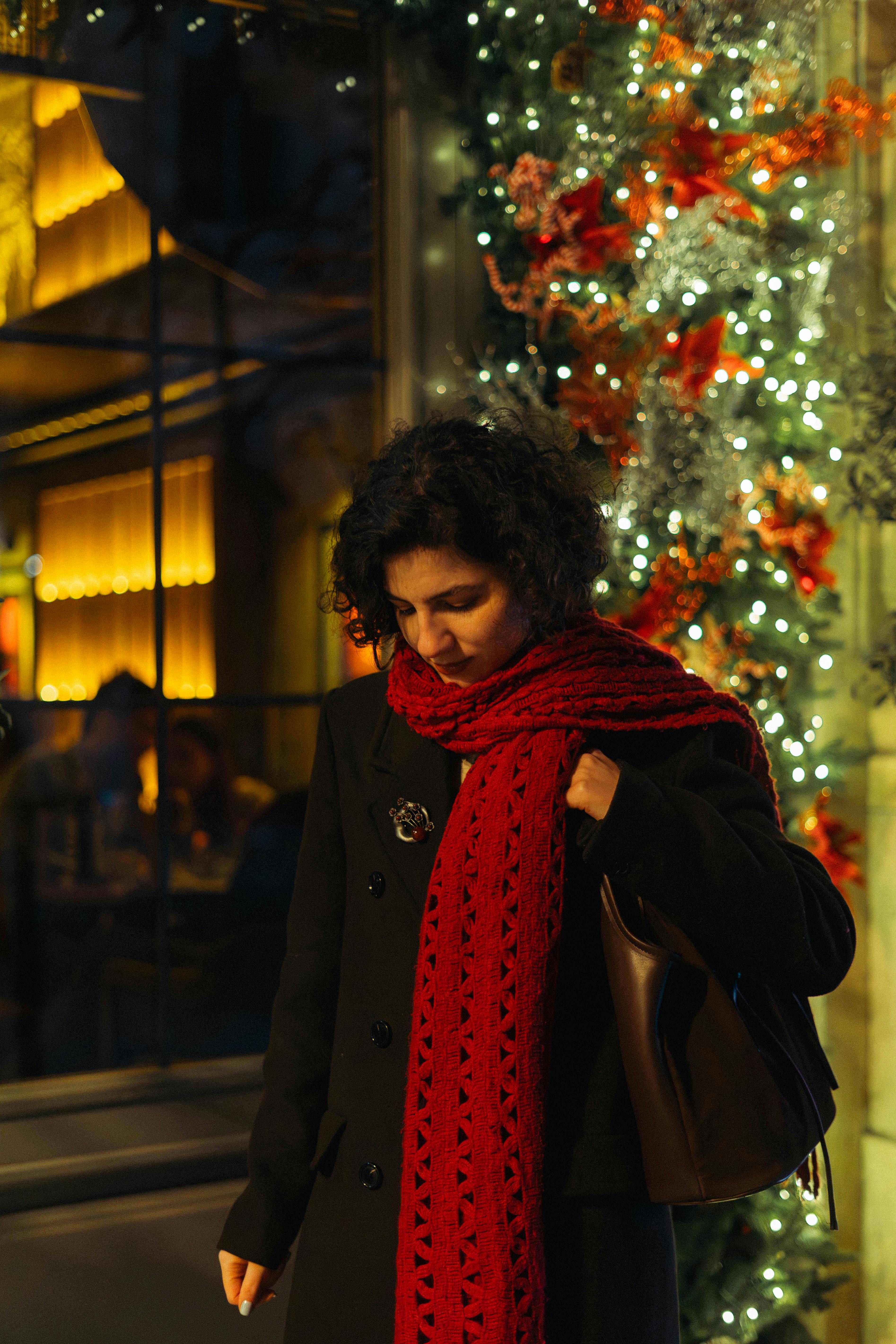 Bezpłatne Kobieta stoi przy oświetlonym oknie z czerwonym szalikiem, na tle przytulnej nocnej scenerii w Baku. Zdjęcie z galerii