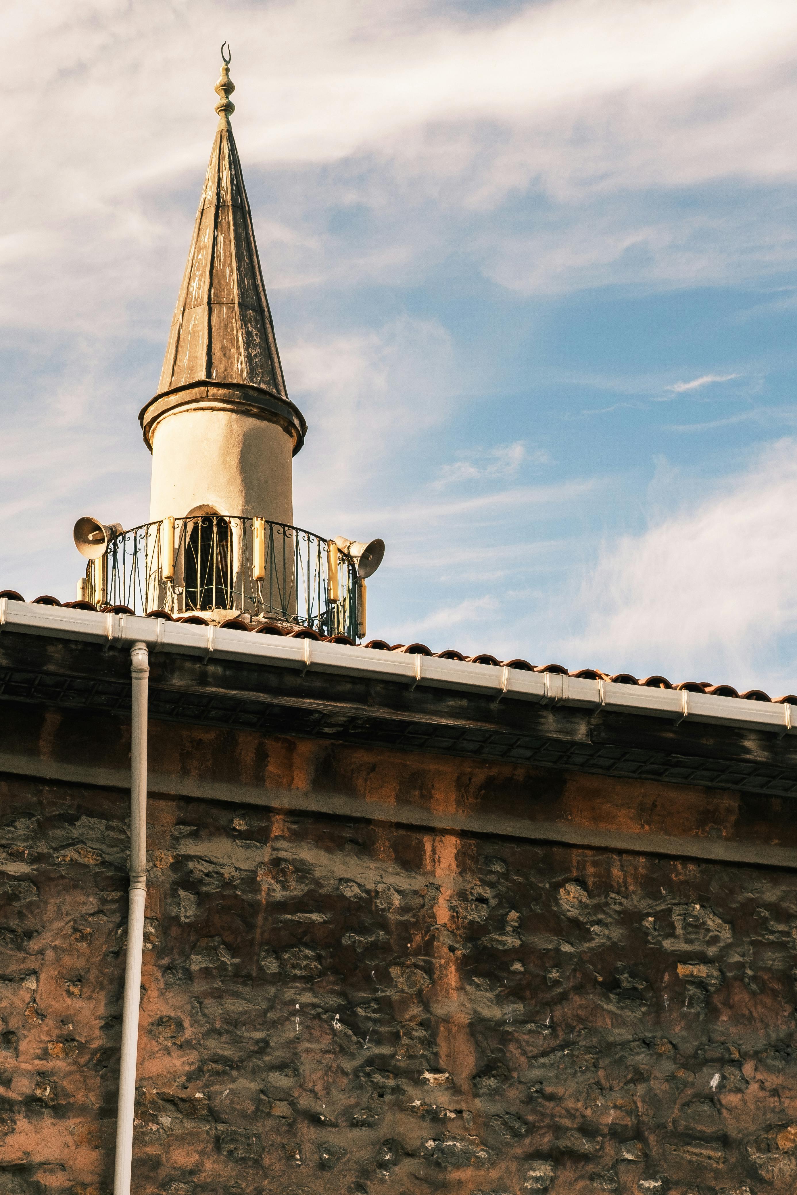 бесплатная Вид сверху на старинное каменное здание с минаретом под ярко-голубым небом. Стоковое фото