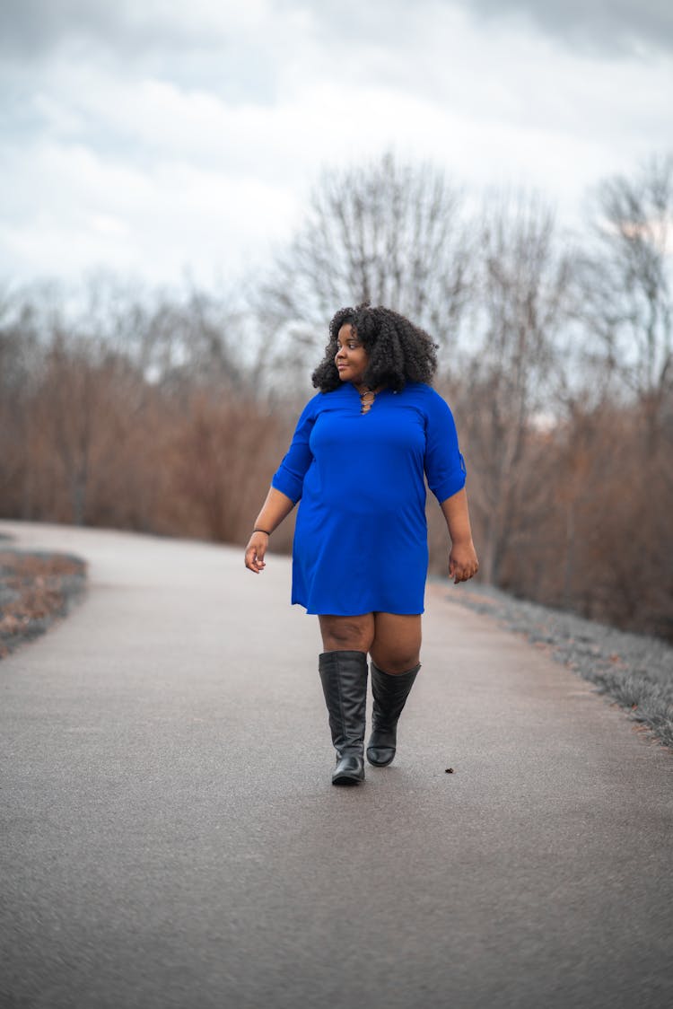 Woman In Blue Dress And Black Boots Walking Alone On Empty Road