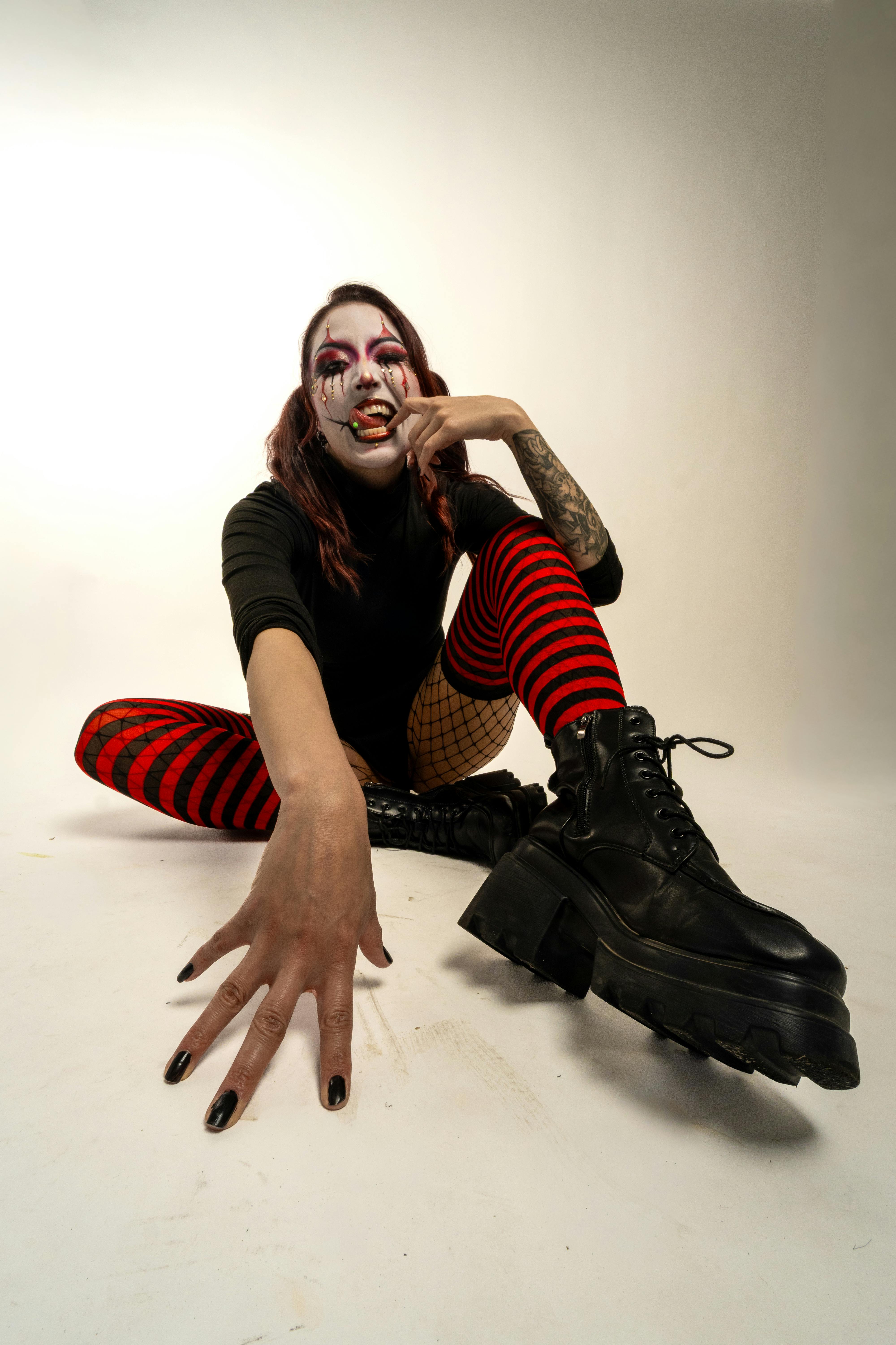 無料 芸術的なカーニバルメイクを施し、赤と黒の縞模様の衣装を身に着けた女性が屋内でポーズをとっています。 写真素材