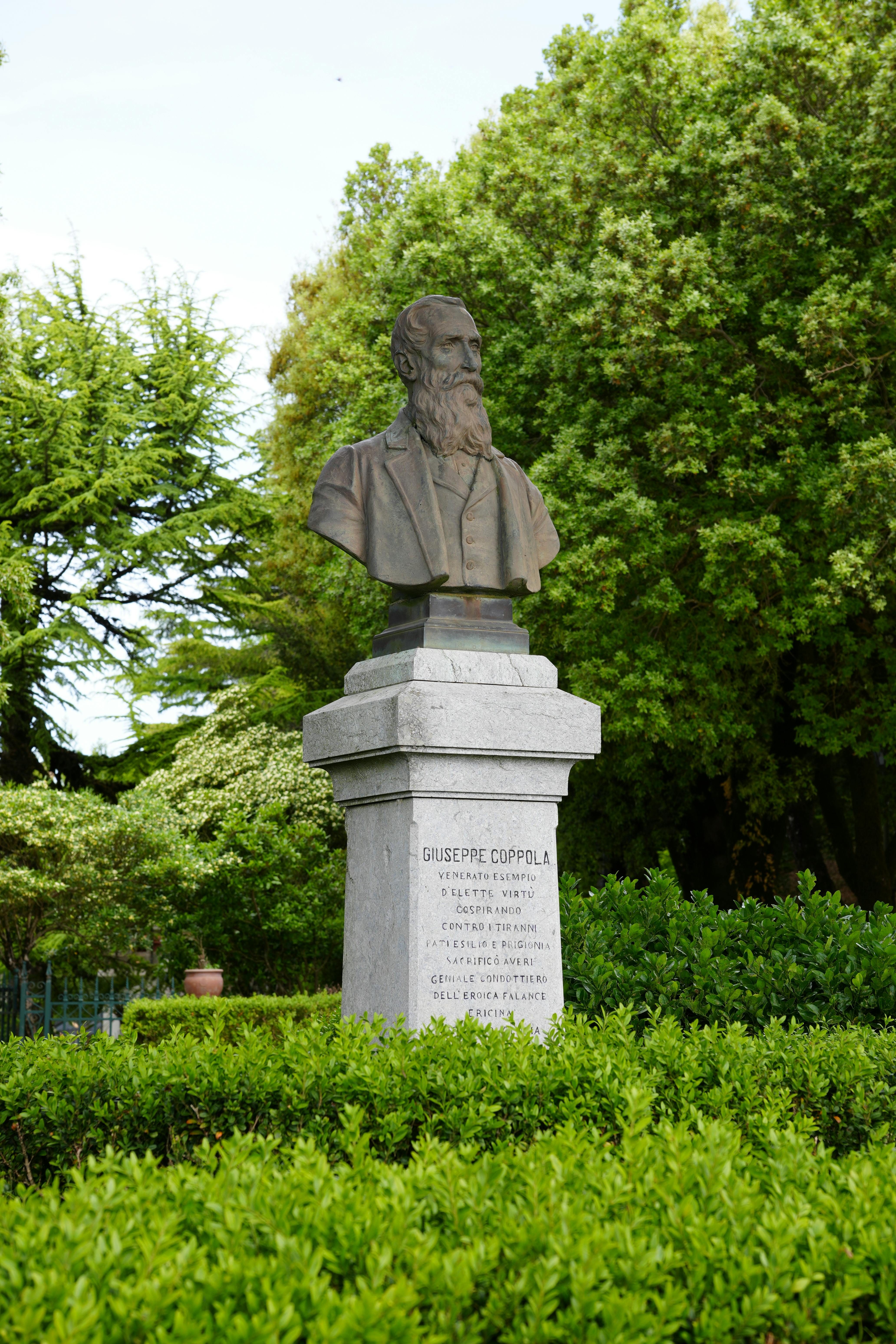 Bust of Giuseppe Coppola in a tranquil park setting in Erice, Sicily, Italy.