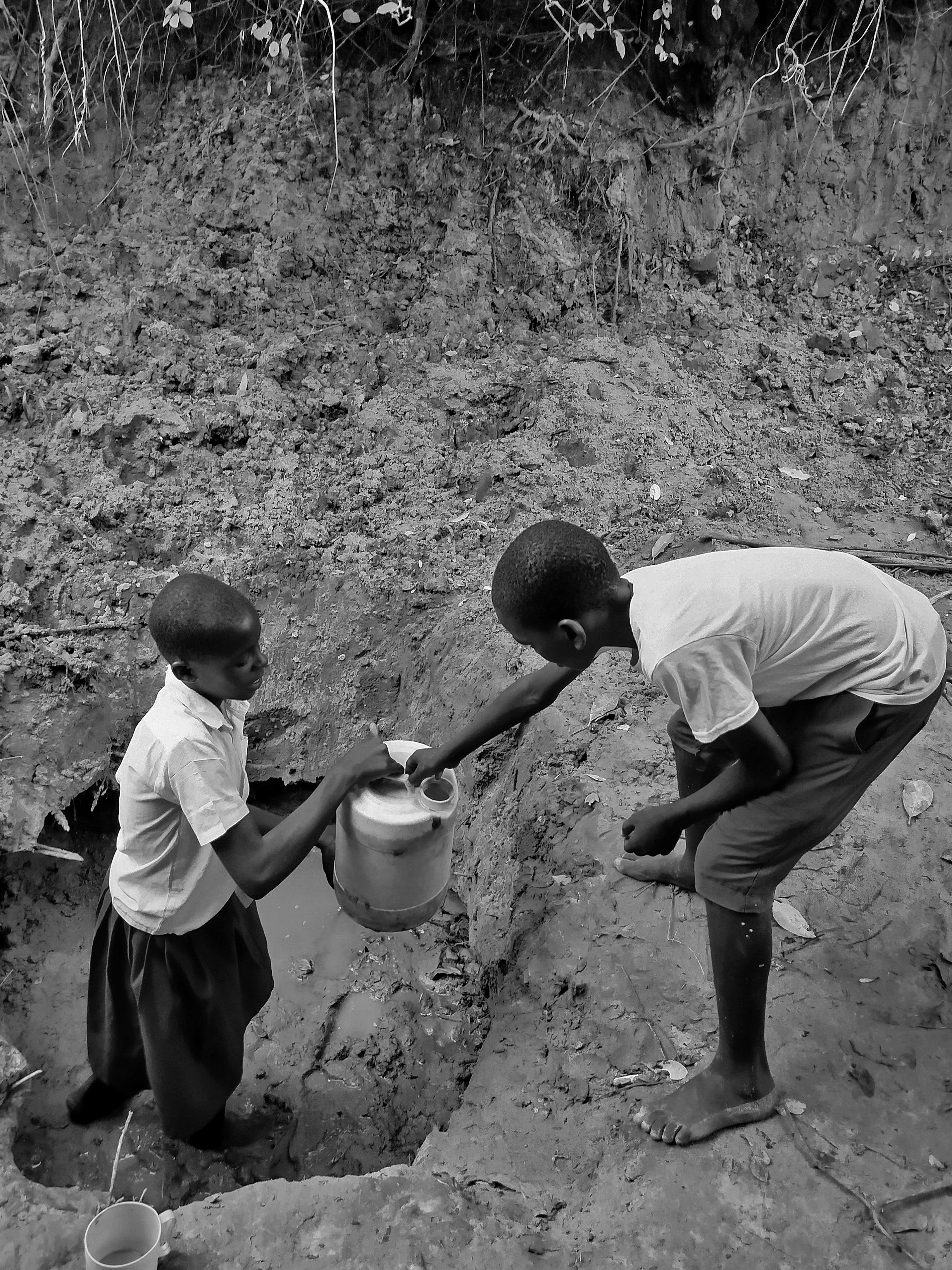 Two children gather water from a dry riverbed, highlighting water scarcity issues.