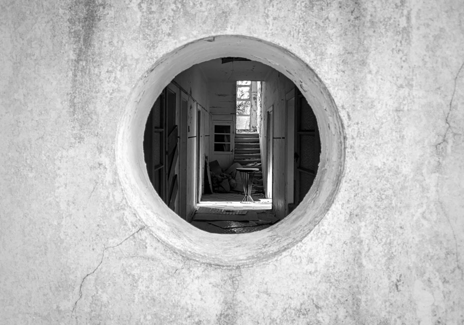 Artistic black and white photo through a round window into an abandoned hallway.