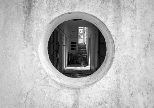 Free Artistic black and white photo through a round window into an abandoned hallway. Stock Photo