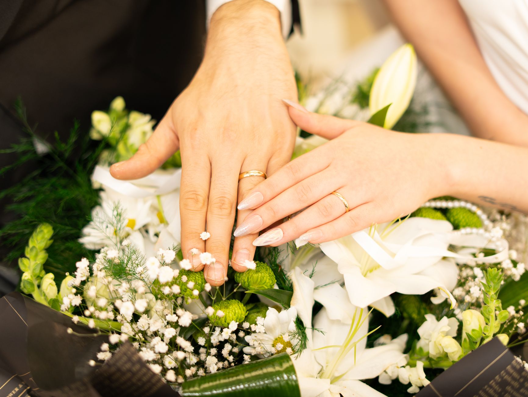Close-up of hands with wedding rings resting on a bouquet, symbolizing matrimonial unity.