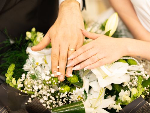Free Close-up of hands with wedding rings resting on a bouquet, symbolizing matrimonial unity. Stock Photo