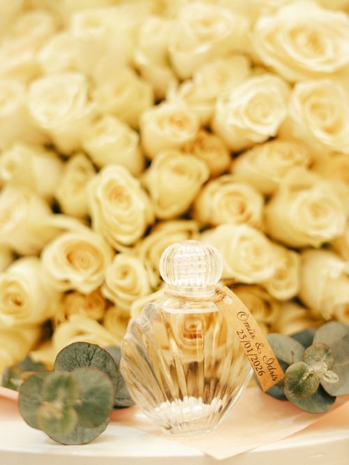 Free Crystal perfume bottle with cream roses background and eucalyptus accents, perfect for weddings. Stock Photo