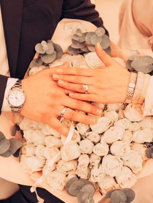 Free Close-up of wedding rings on couple's hands with a pastel floral bouquet background. Stock Photo