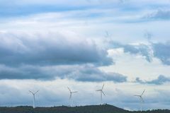 Scenic view of wind turbines on a hill with a cloudy sky, representing renewable energy.