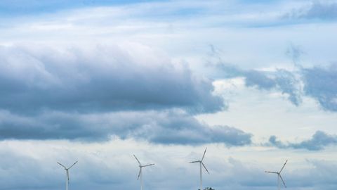 Scenic view of wind turbines on a hill with a cloudy sky, representing renewable energy.