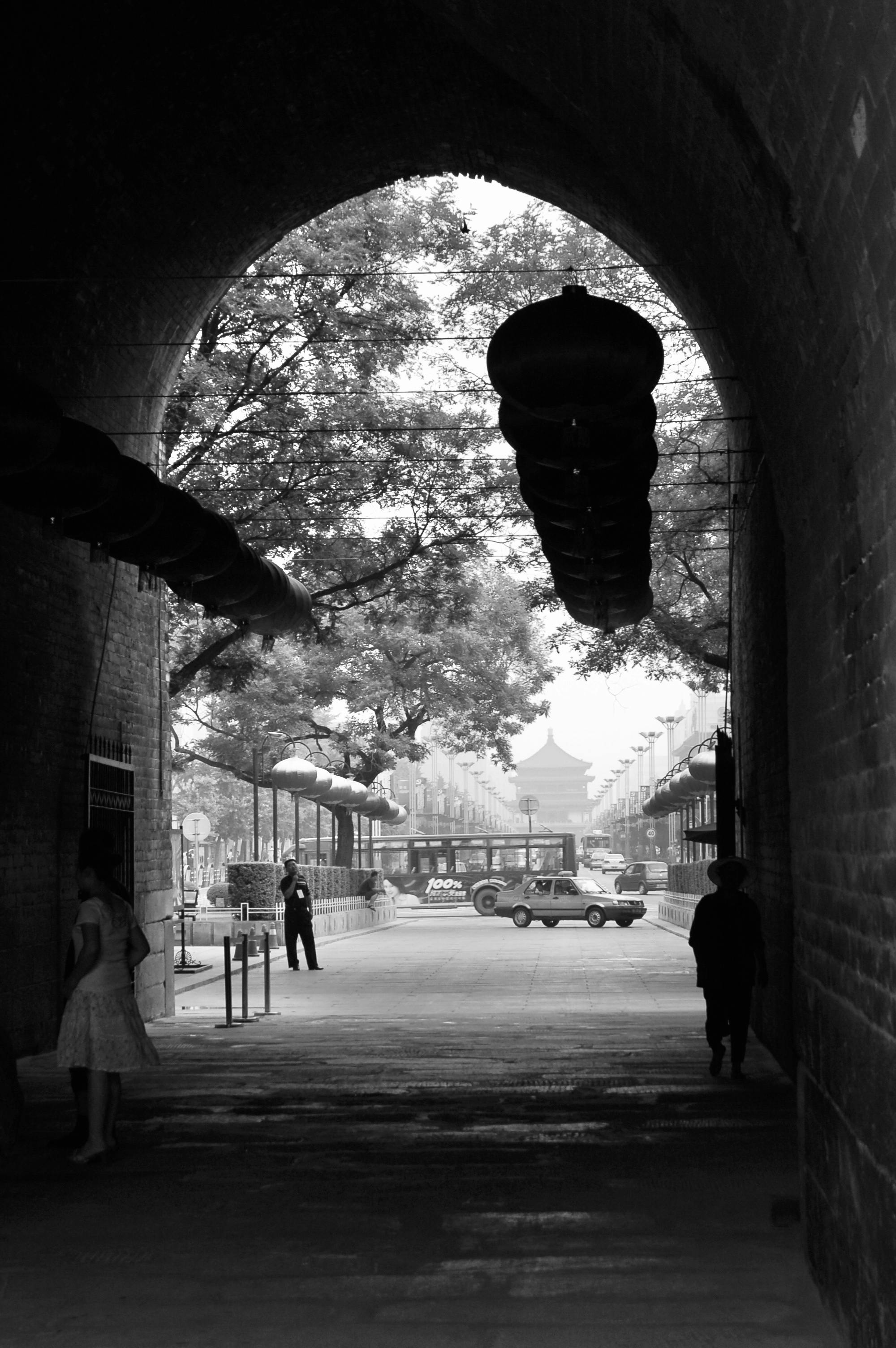 Free A black and white photo of a bustling urban street viewed through an archway adorned with lanterns. Stock Photo