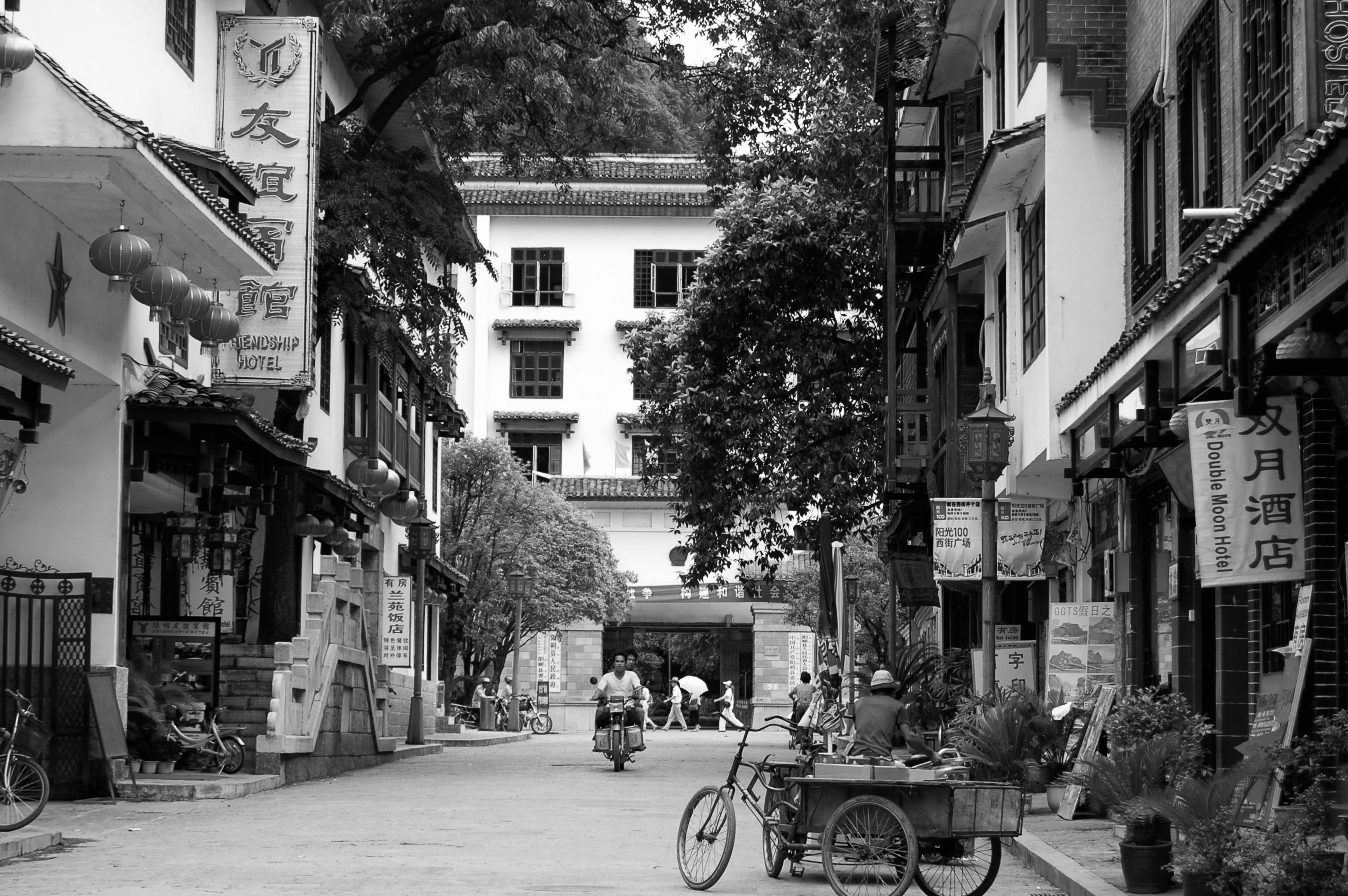 Gratis Pemandangan hitam putih sebuah jalanan tradisional Asia yang ramai dengan toko-toko dan sepeda. Foto Stok