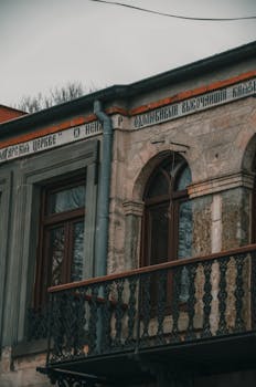 A vintage stone building with ornate balcony and arched windows in moody lighting.