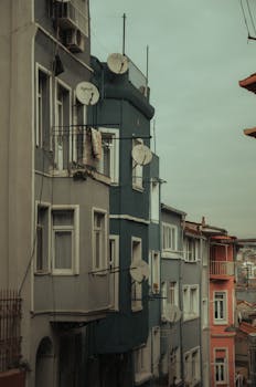 Colorful city apartments with satellite dishes line a narrow street, showcasing urban architecture.