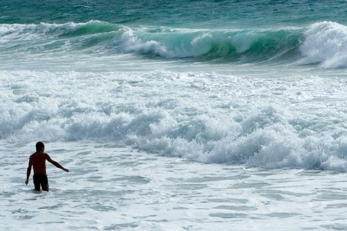 Free A man wades into the crashing ocean waves on a sunny day. Stock Photo