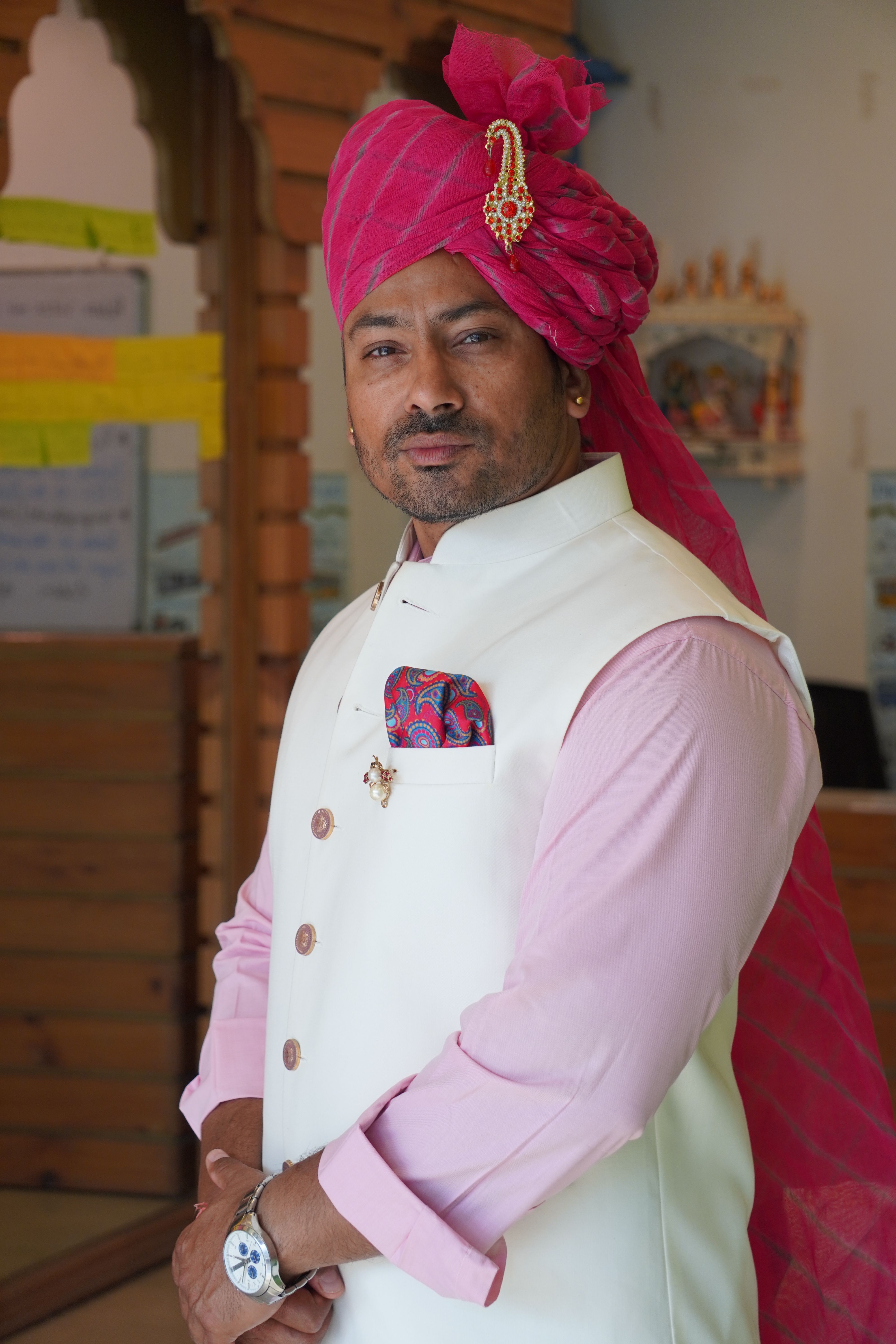 A man in traditional Indian attire with a vibrant pink turban poses confidently indoors.