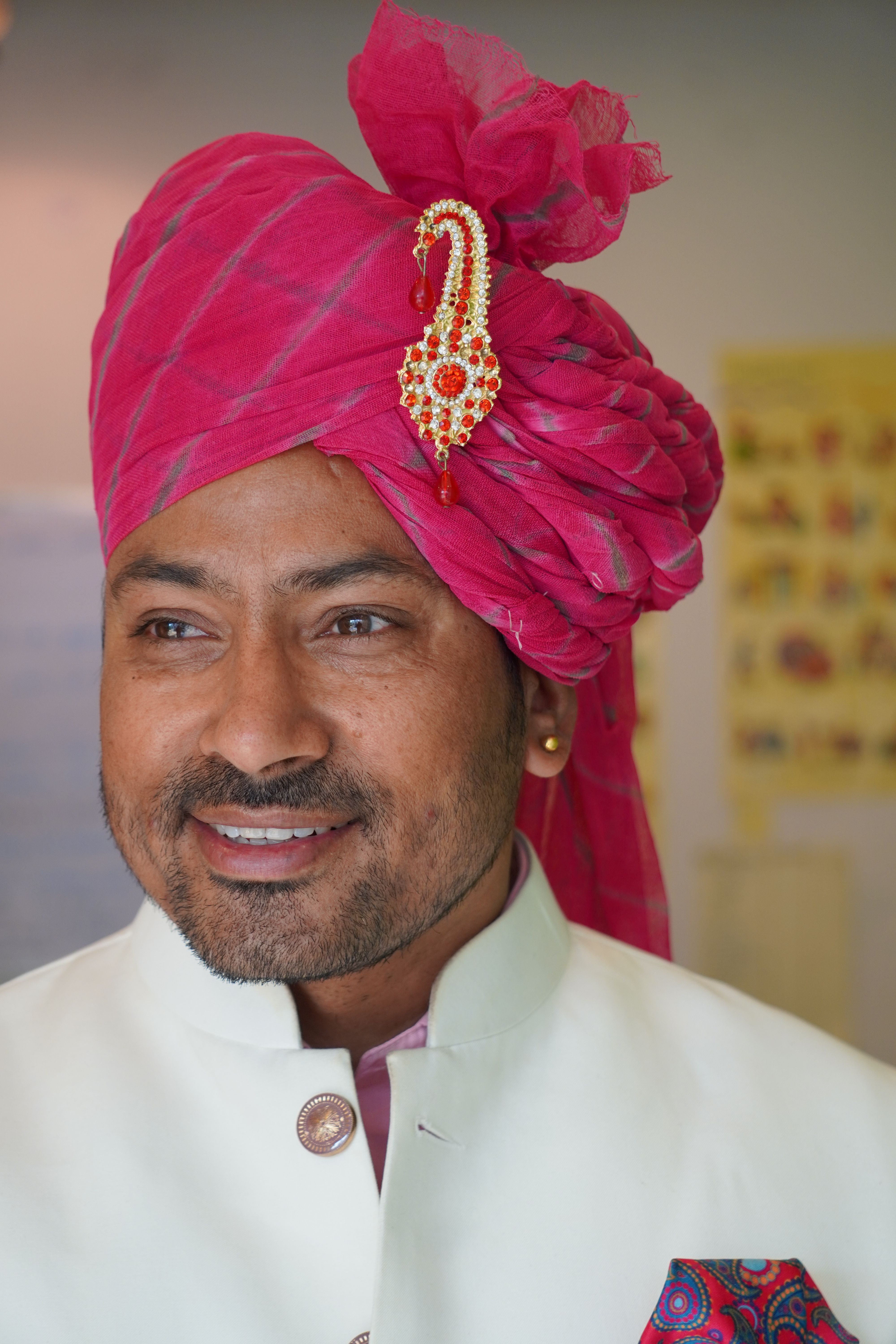 Smiling man in Indian attire with pink turban indoors, signifying cultural heritage.