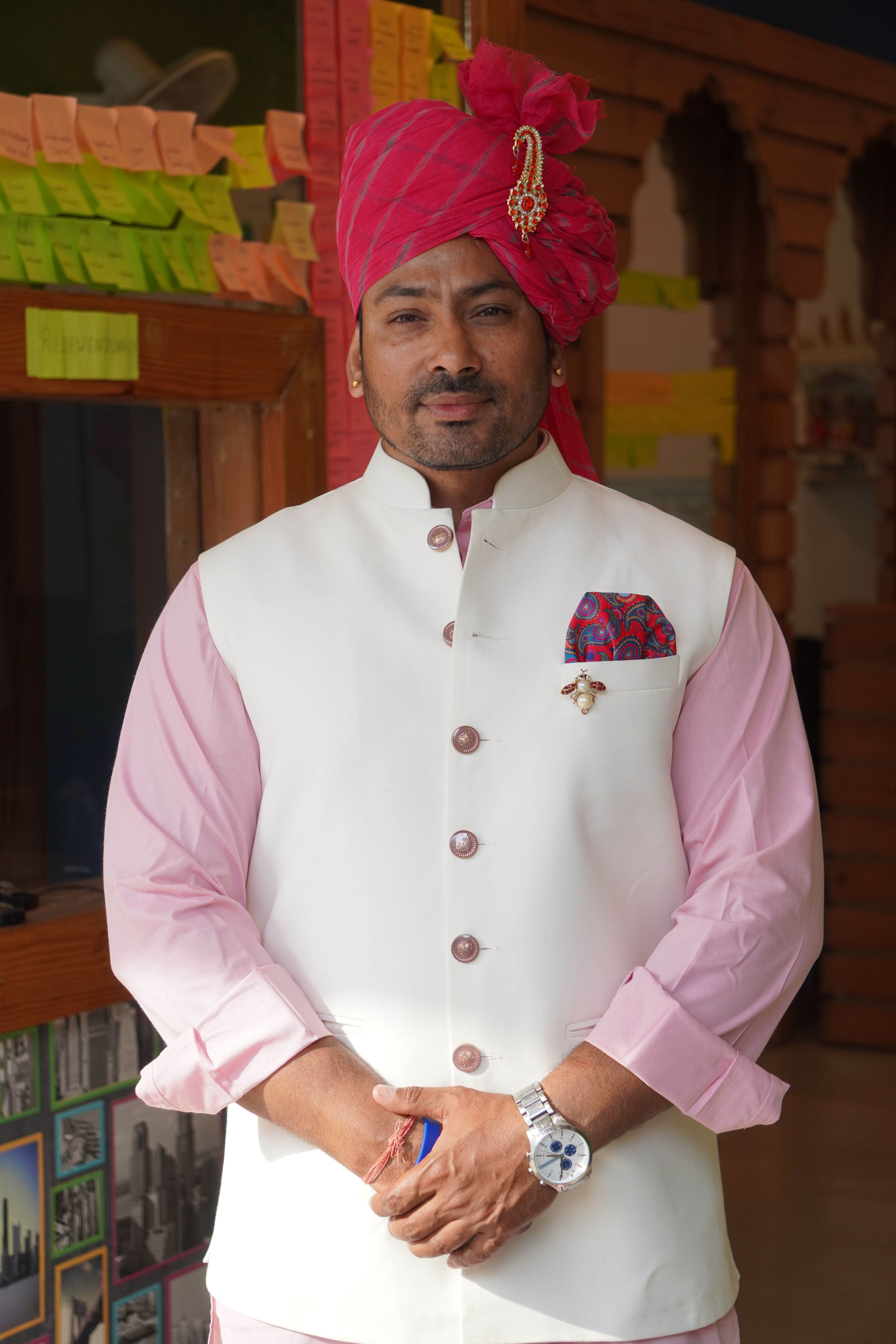 Man in traditional Indian attire with pink turban and white vest indoors with colorful post-it notes.