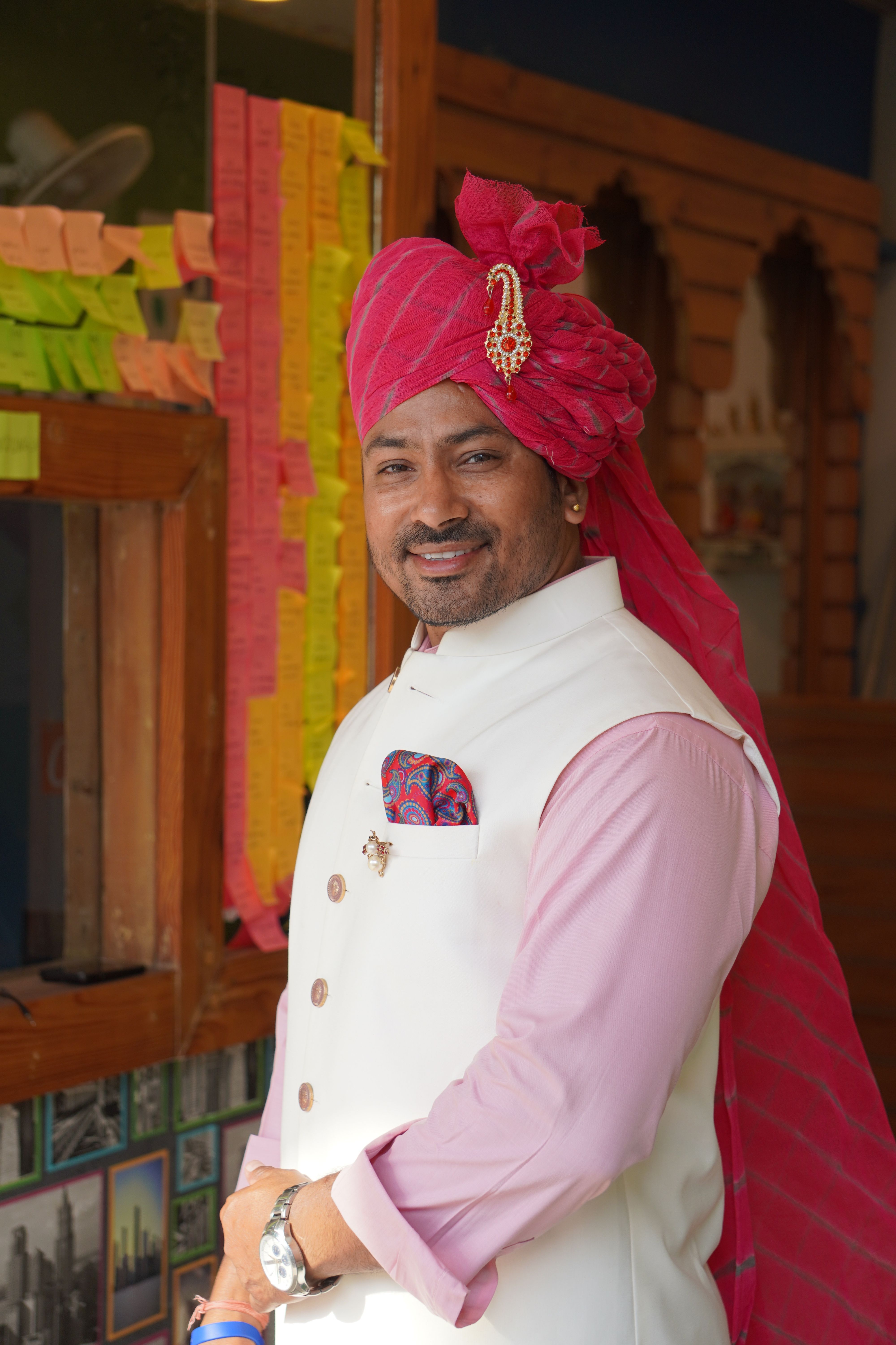 Portrait of a man wearing traditional Indian clothing with a turban, smiling indoors.