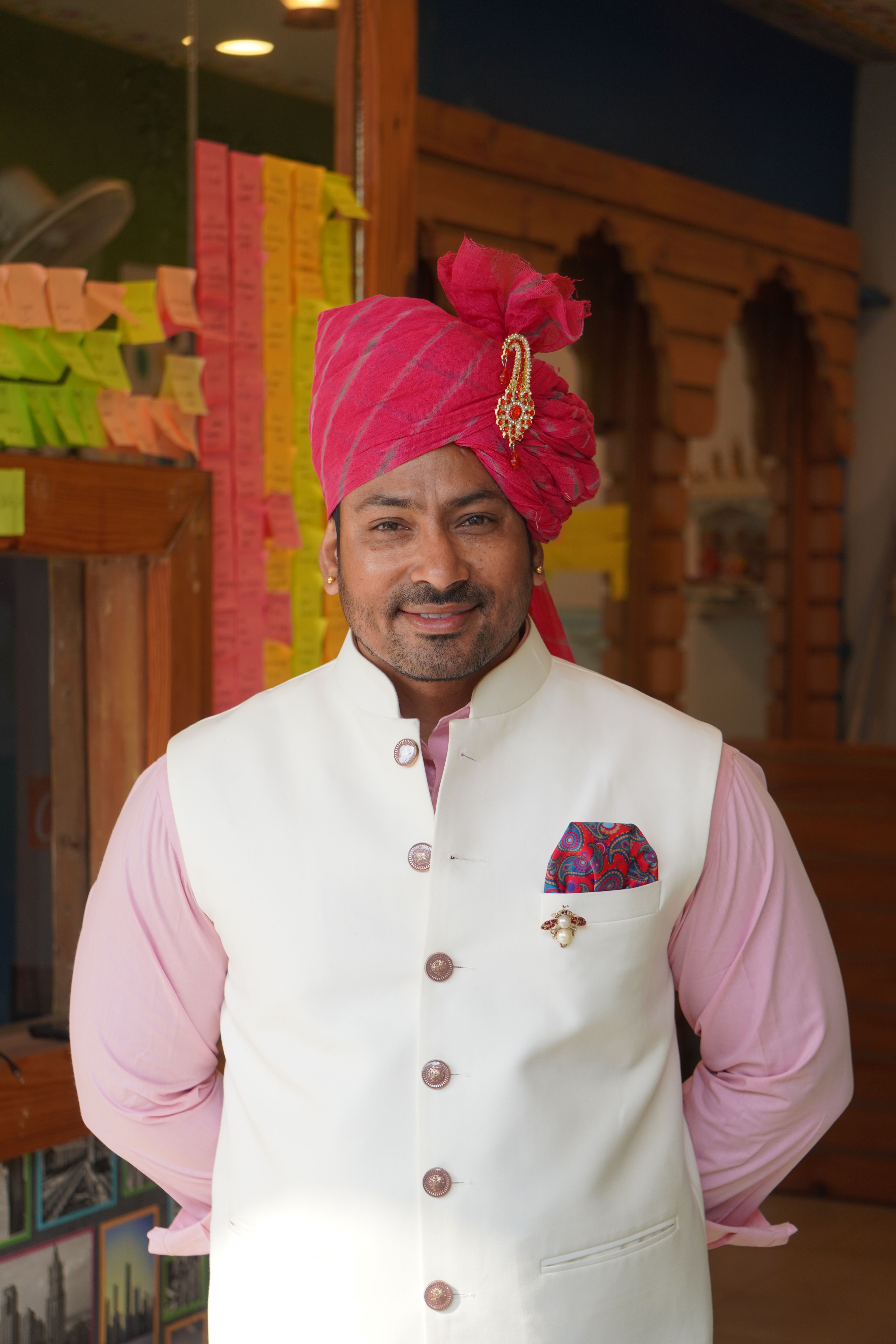 Smiling man wearing traditional Indian turban and vest indoors, adding cultural charm.