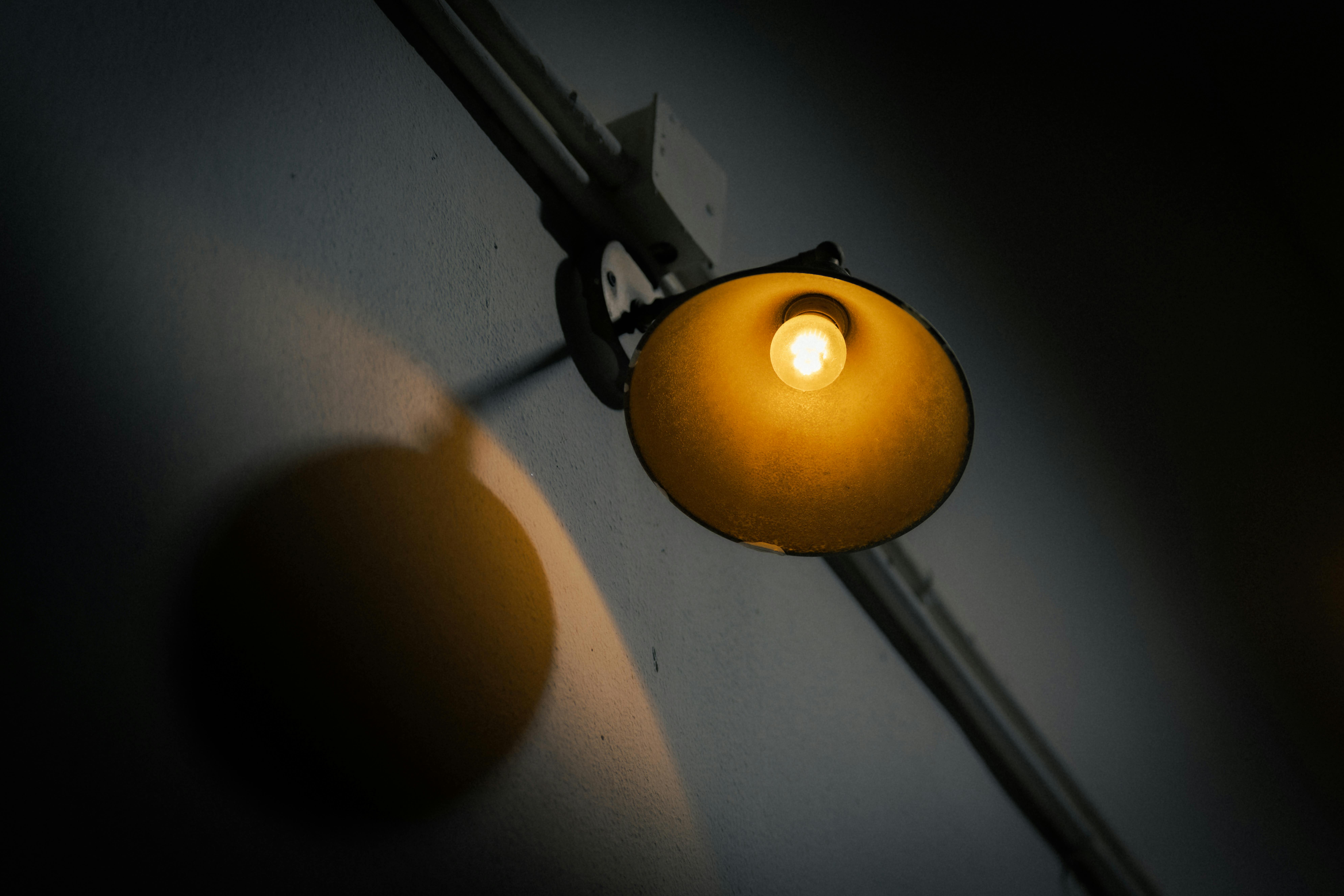 Gratis En enkelt vægmonteret lampe skaber en varm og stemningsfuld atmosfære i mørke indendørs omgivelser. Lagerfoto