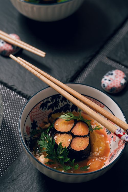 Free Japanese dish garnished with herbs, served with chopsticks in a decorative bowl. Vibrant and appetizing. Stock Photo