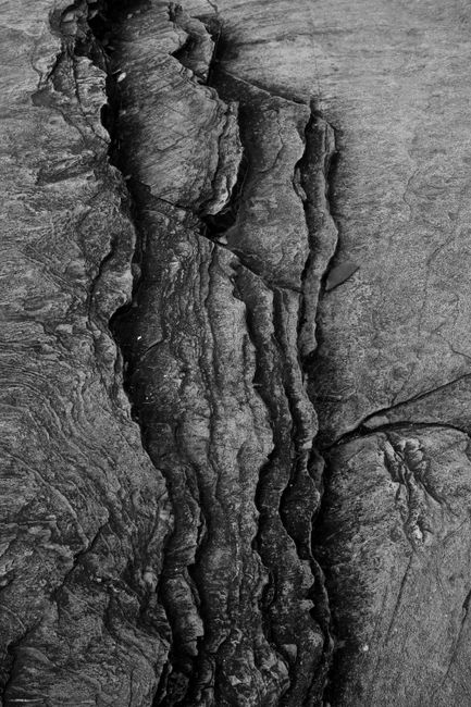 Close-up of a cracked rock surface with intricate textures, captured in black and white.