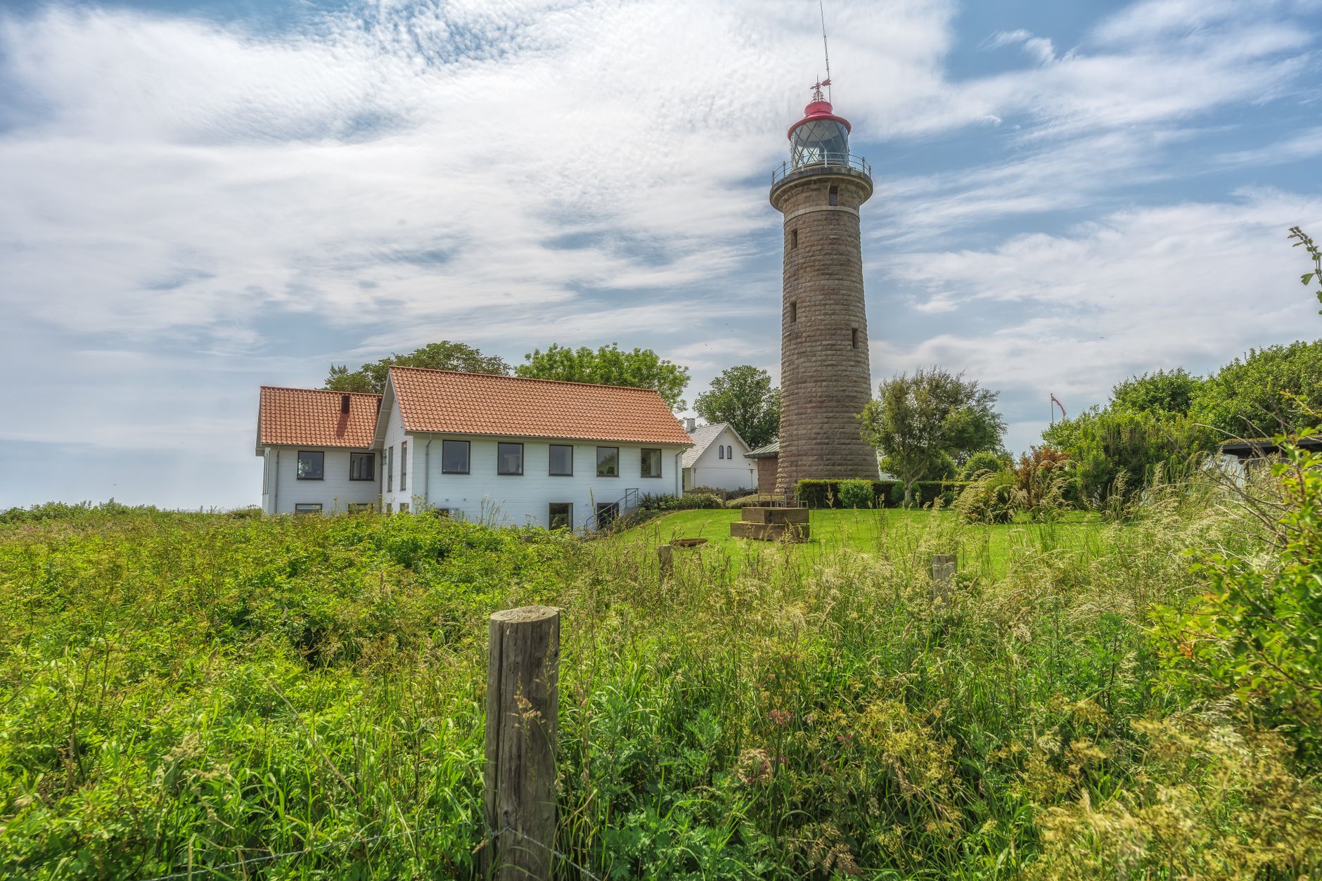 Scenic view of a lighthouse and cottage surrounded by lush greenery under a bright blue sky.