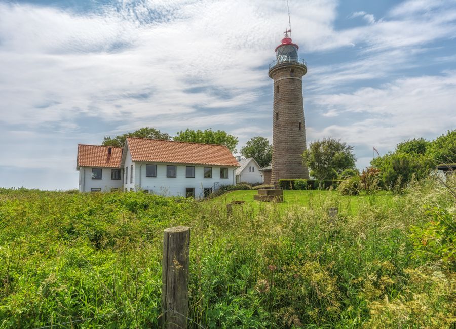 Scenic view of a lighthouse and cottage surrounded by lush greenery under a bright blue sky.