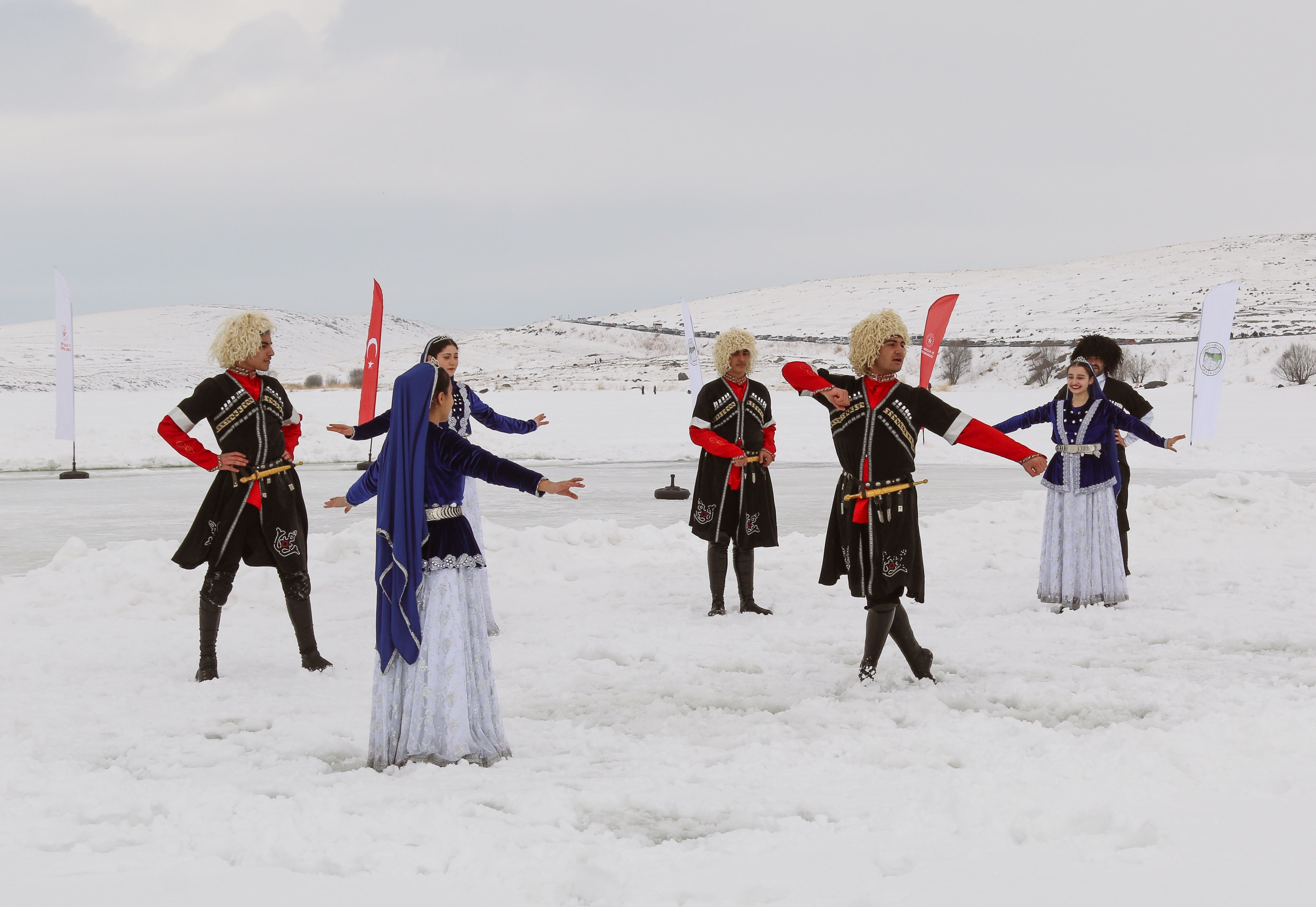Performers in traditional costumes dancing on snow in Türkiye, showcasing cultural heritage.