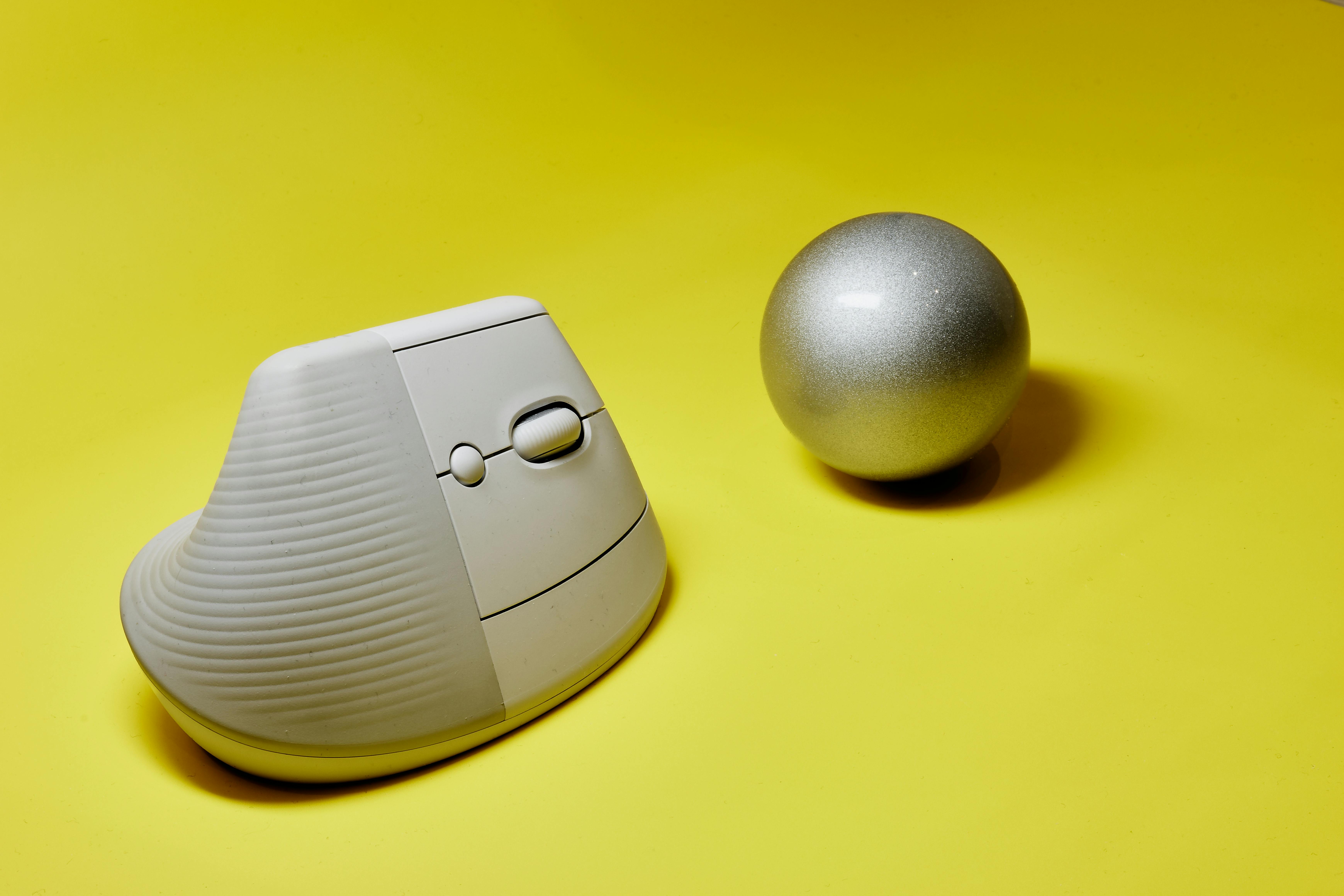 Free A sleek ergonomic vertical mouse next to a metallic sphere on a vibrant yellow background. Stock Photo